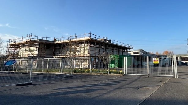 Exterior view of a school building covered in scaffolding with a metal fence in the foreground