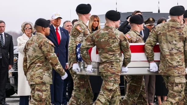 Members of a US Army carry team transport a flag-draped coffin of those killed in Kuwait as US President Donald Trump salutes.