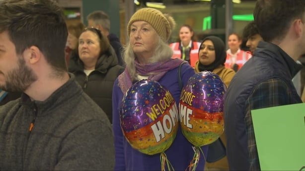 A woman stands with Welcome Home balloons in Dublin Airport