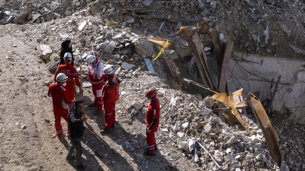 Civilians and emergency workers stand near the remains of a residential and commercial building in Tehran, Iran