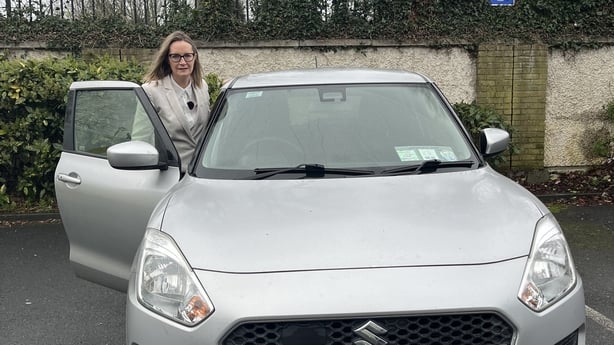 A woman poses for a photograph as she gets into a silver coloured car