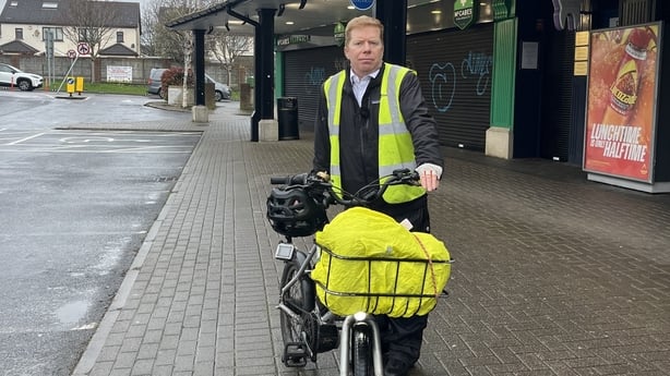 a man wearing a hi-vis vest poses for a photograph with his bicycle 
