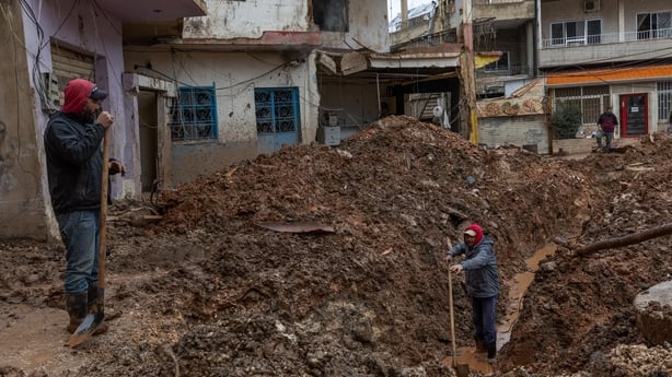 Two men with shovels stand inside and on top of a large crate created by a missile strike