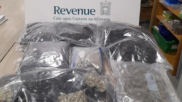 Image shows a table displaying several clear plastic bags containing herbal cannabis