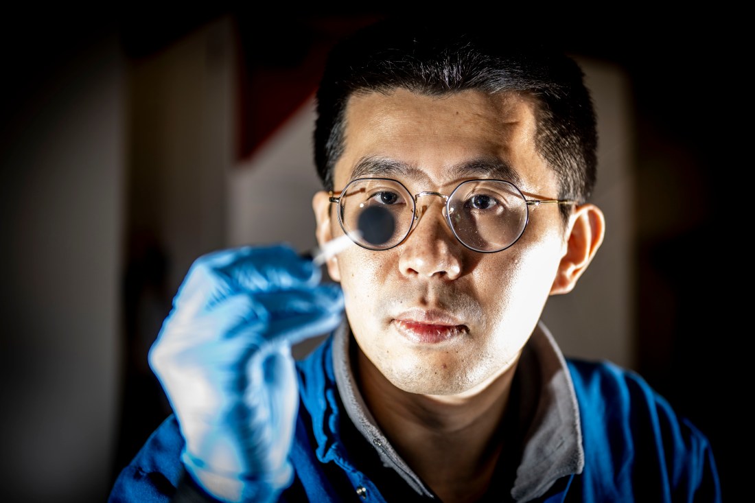 Researcher Juner Zhu, wearing safety glasses and gloves, reaches into a lab chamber while working on electric vehicle battery research at Northeastern’s Kostas Research Institute in Burlington, Massachusetts.