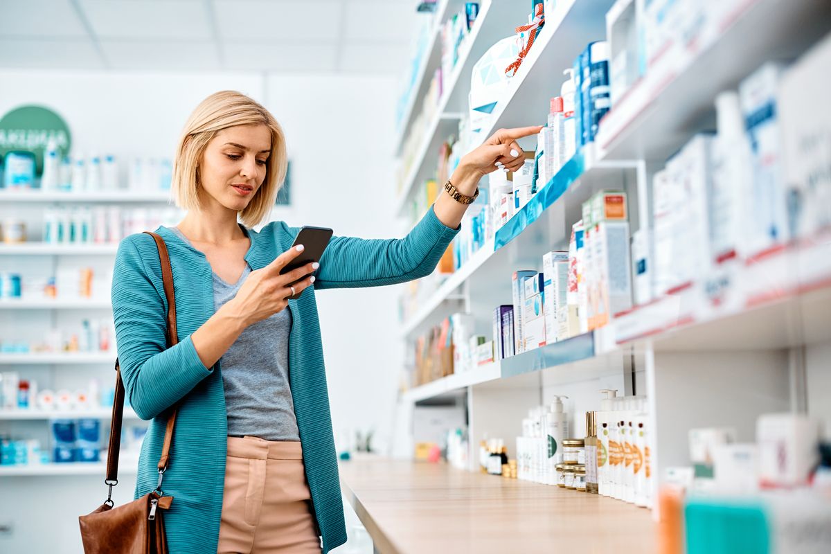 Smiling woman searching for medicine while using mobile phone in drugstore.