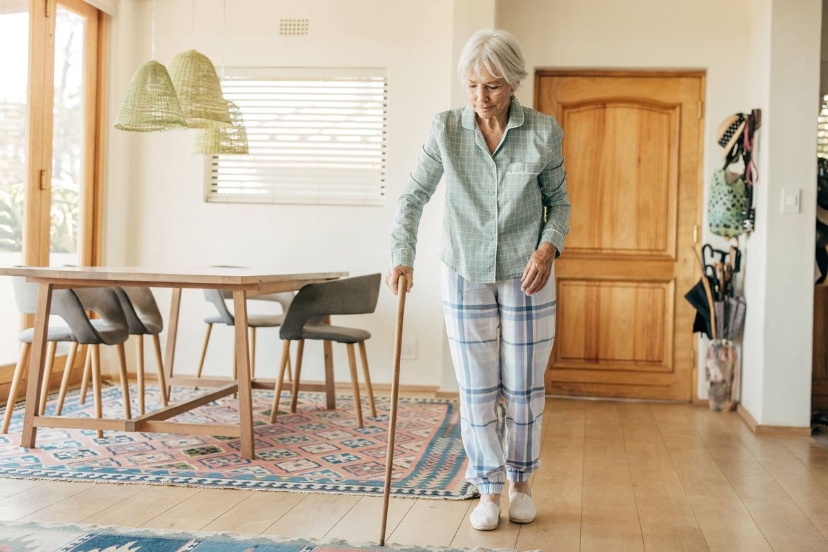 Senior woman practicing mobility in a cozy home setting, using a walking stick for support and stability.
