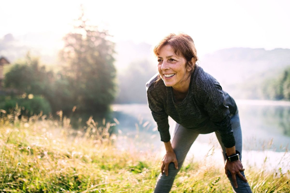 Senior woman resting after exercise outdoors in nature in the foggy morning. Copy space.