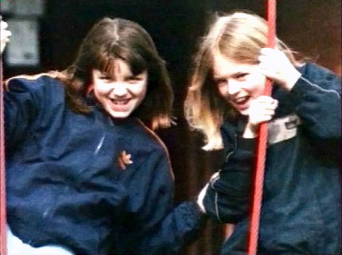 Two individuals dressed in matching navy blue athletic jackets are standing side by side, gripping red poles, and sharing a joyful moment, possibly engaged in a recreational activity.