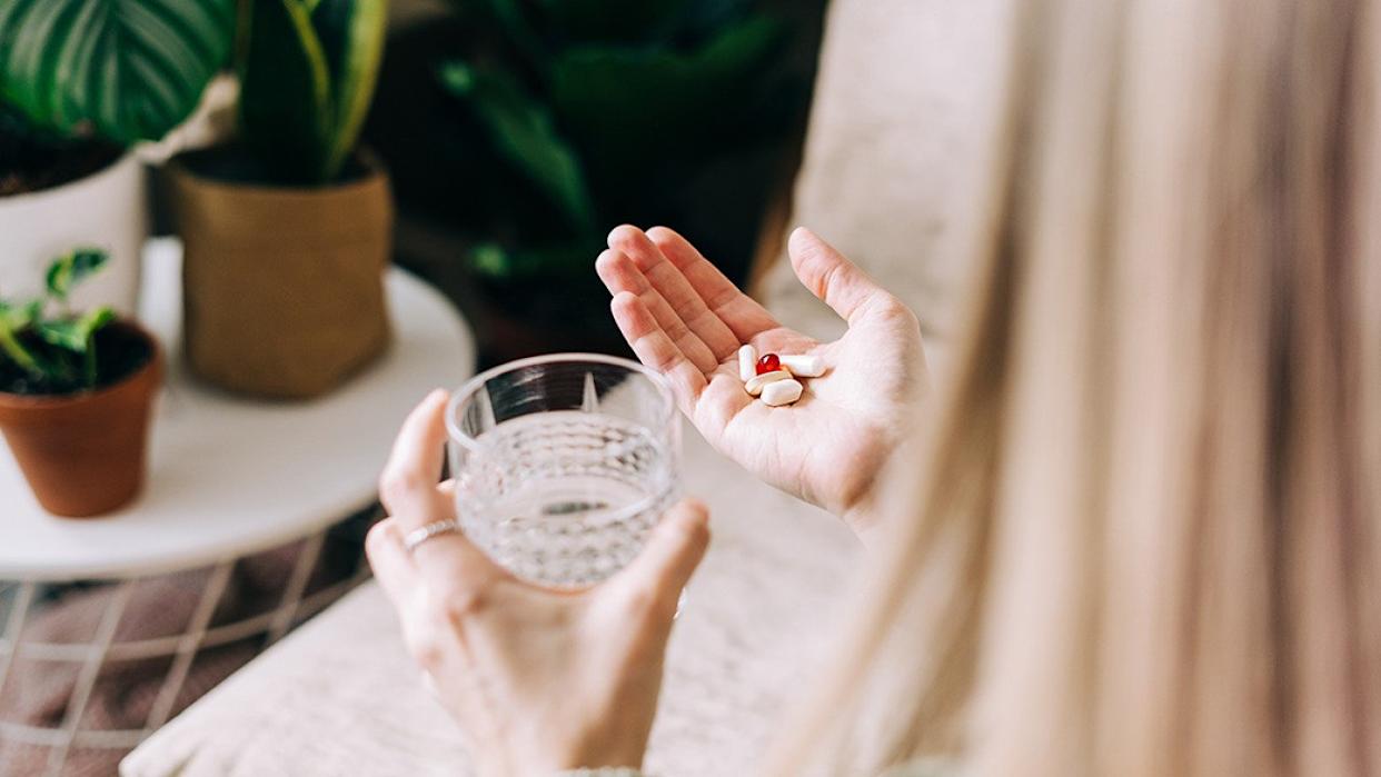 A woman holding multiple pills to drink with a glass of water. - Ostanina Anna // Shutterstock