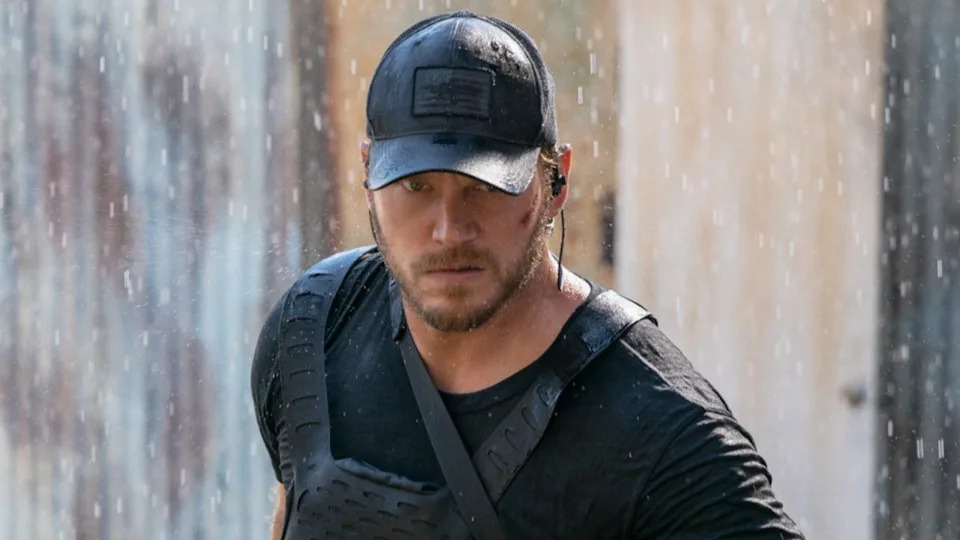 Chris Pratt looking mad and walking forward with a baseball hat on in the rain. .