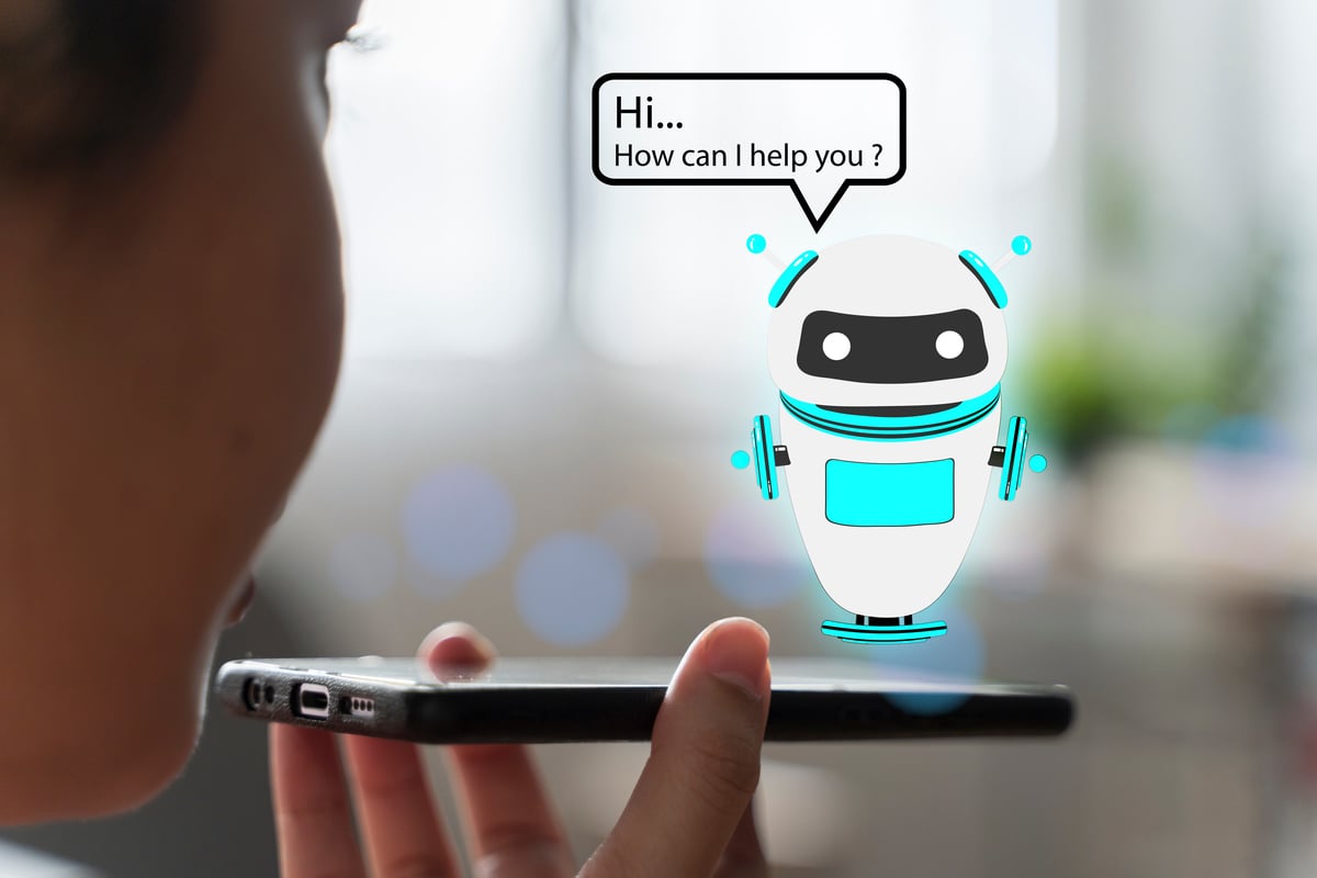 A person holding a smartphone up to their mouth and a graphic of a little robot with a word bubble reading Hi, How can I help you?