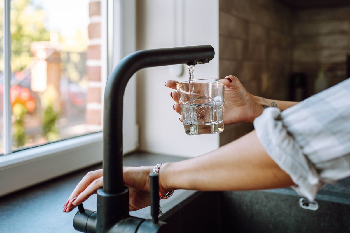 Ensure clean drinking water at home with kitchen filtration. Cropped woman hands filling glass with tap water