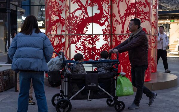 A man pushes children in a cart at a mall in Beijing, Sunday, March 8, 2026. (AP Photo/Ng Han Guan)