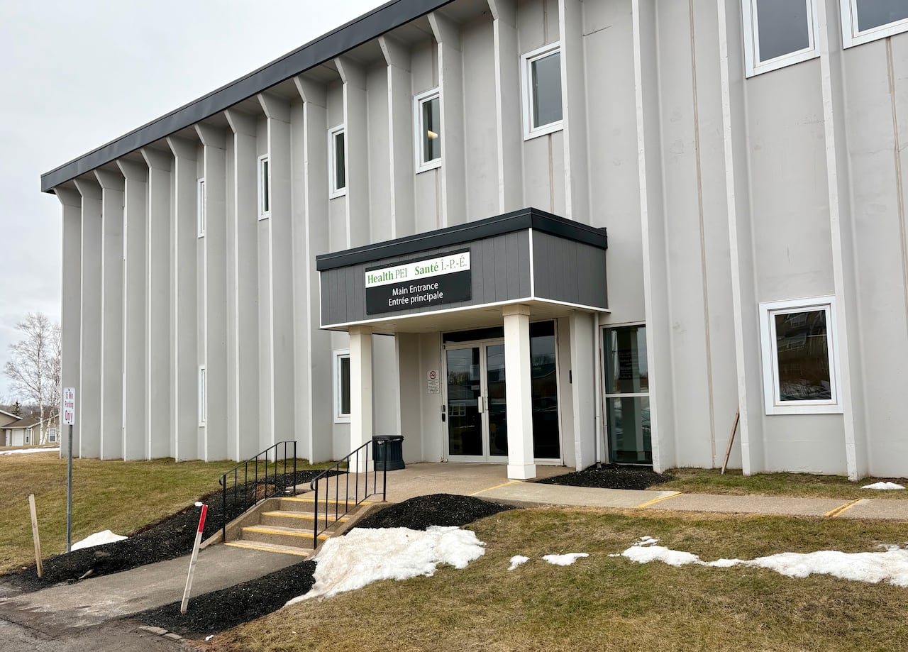 A grey building with a black and white sign and green text is seen outside.