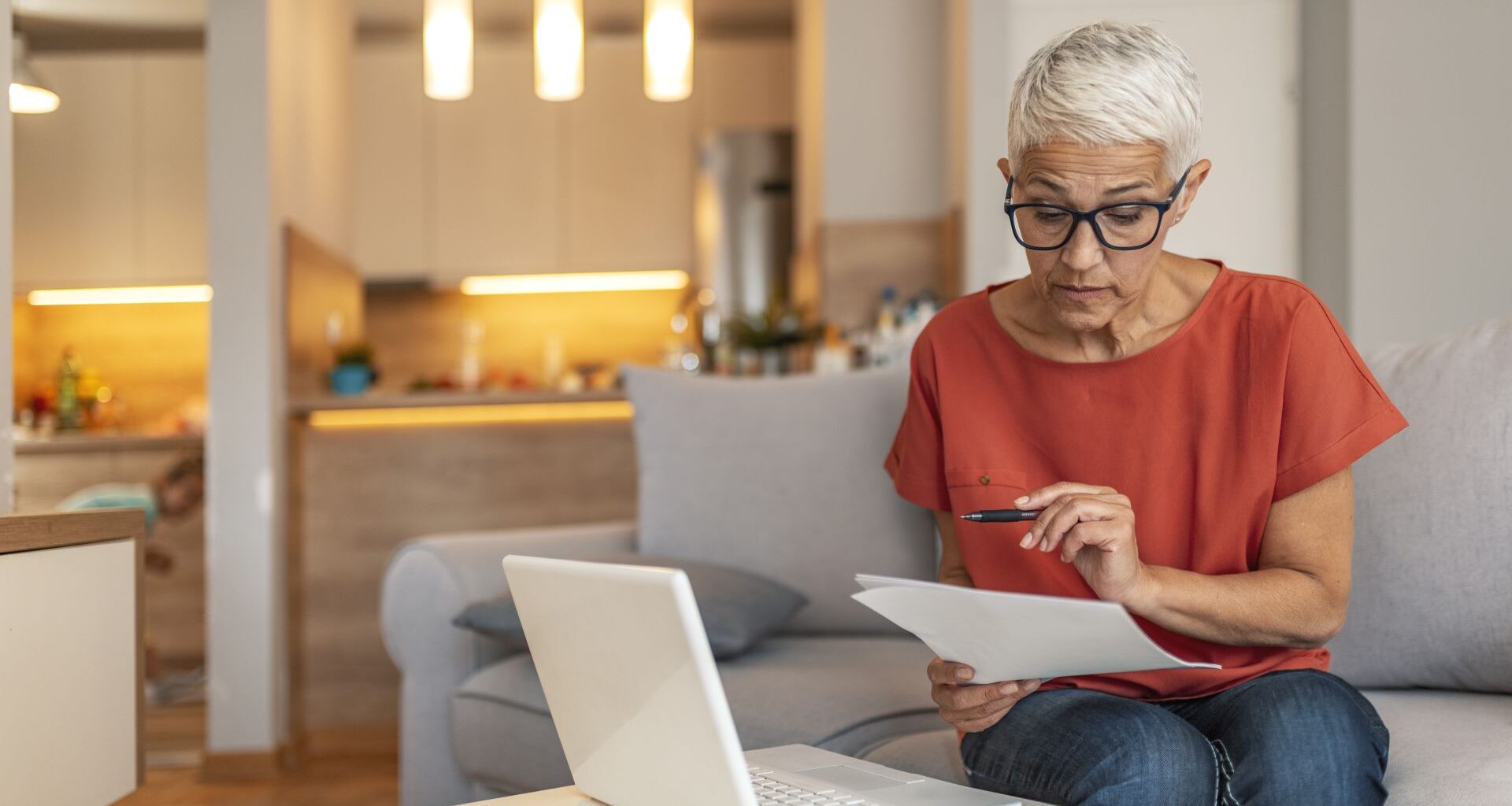 Serious aged woman in eyeglasses checking all bills, calculating expenses.