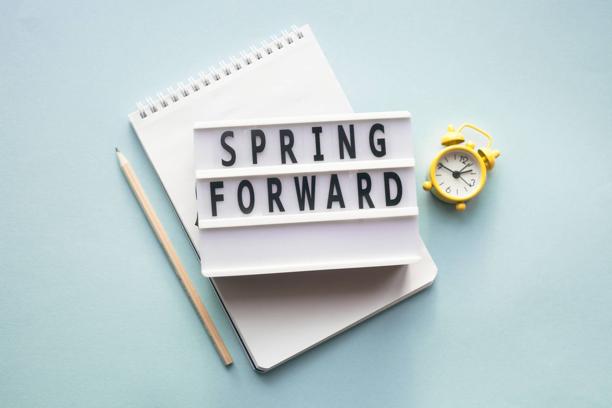 A close-up image displays a notepad with the words "SPRING FORWARD" prominently displayed on top, accompanied by a pencil and a small clock, suggesting an organizational or motivational theme.