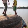 Two children stand on top of an overturned boat along a bank of the Mekong Delta.
