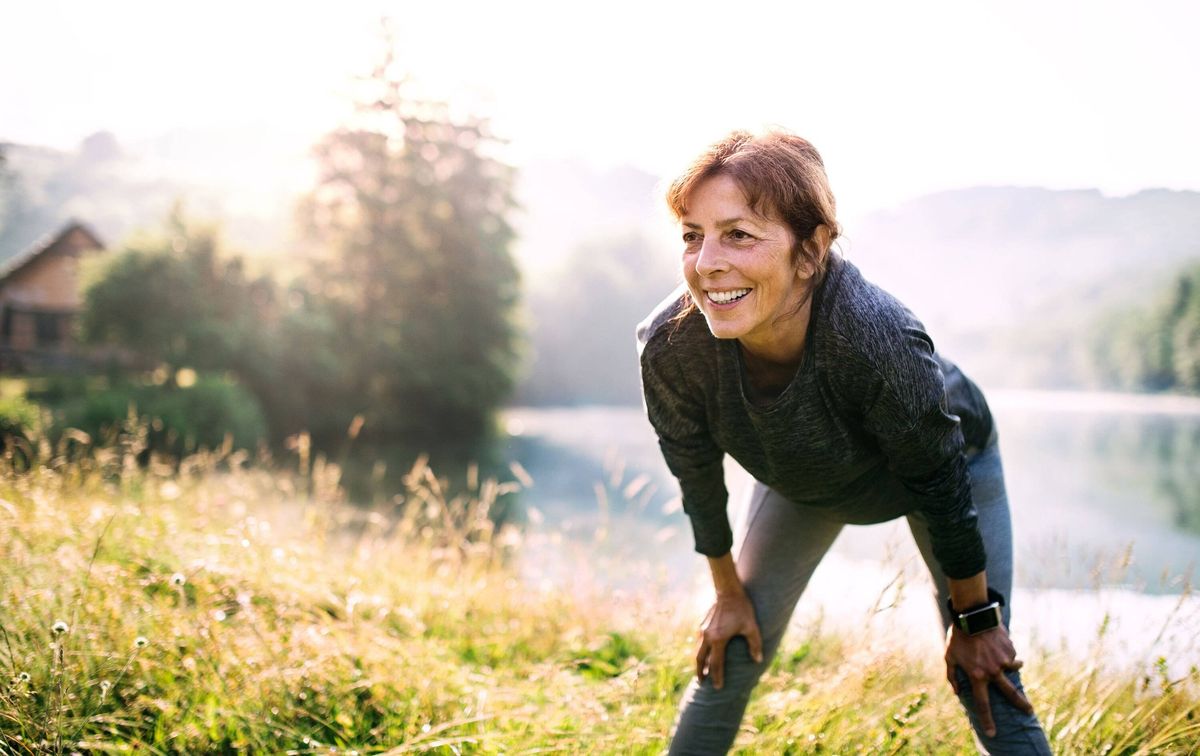 Senior woman resting after exercise outdoors in nature in the foggy morning. Copy space.
