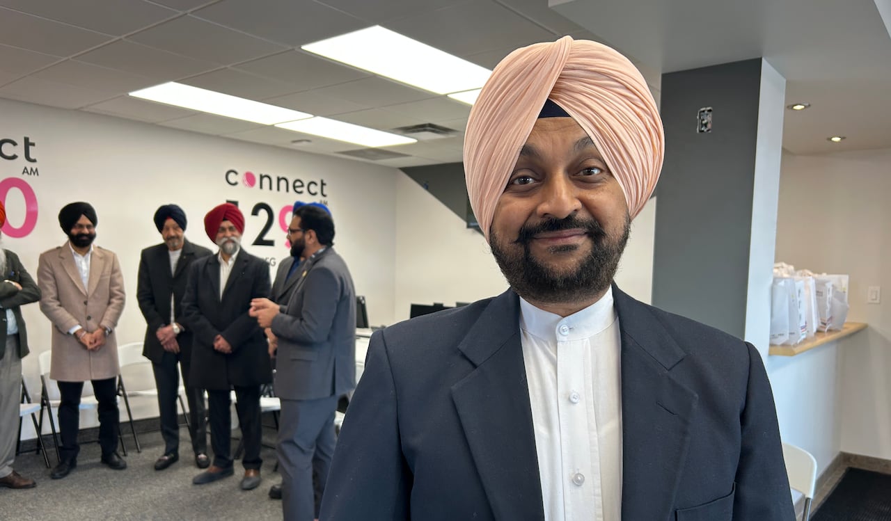 Man with salmon pink turban wears a navy suit and stands in an office room