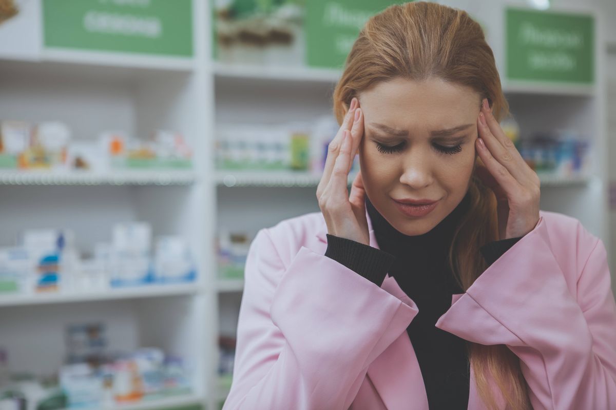 Close up of a young attractive woman having terrible headache, pharmacy on the background. Woman with migraine rubbing temples, 