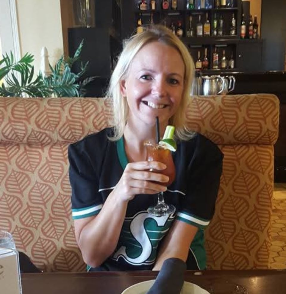 A woman wearing a black and green jersey holds up a drink while sitting in a restaurant booth. 