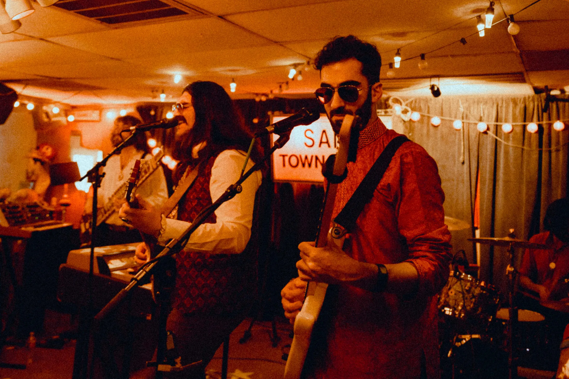 A band performs on stage with orange lighting and string lights.