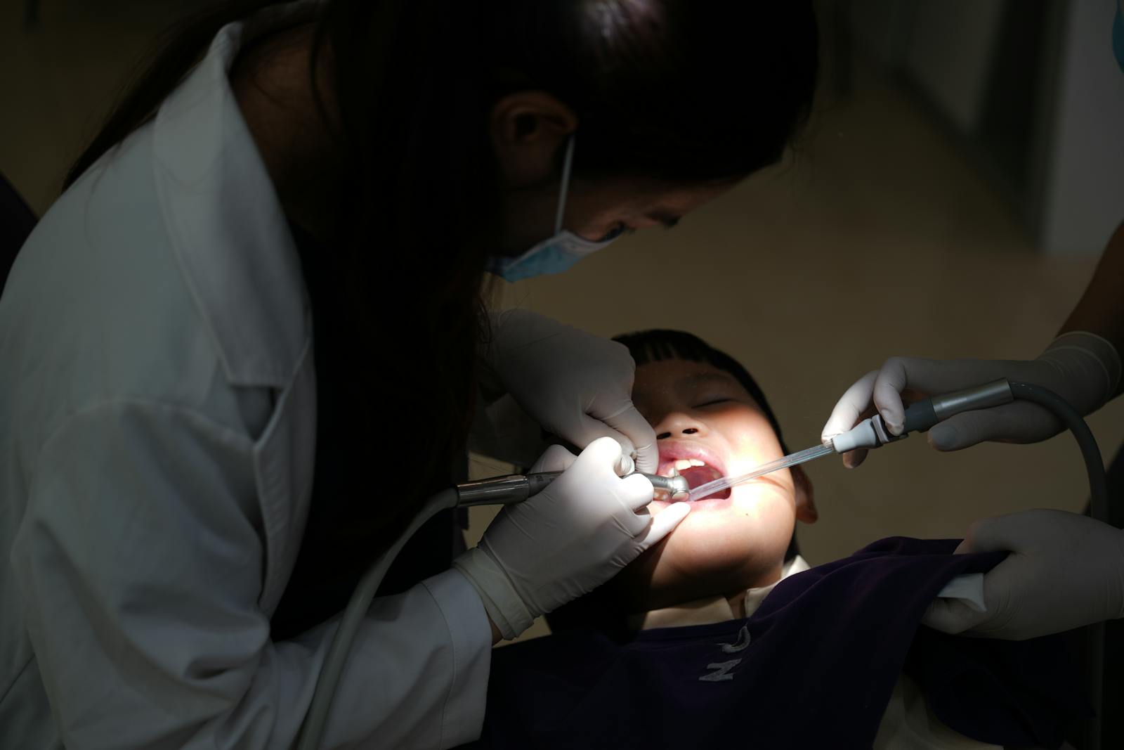 A young child undergoing a dental procedure in a clinic, with a dentist attending.