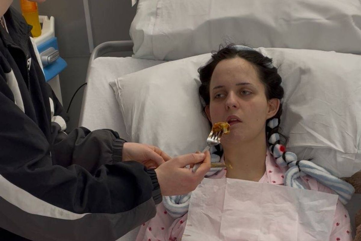 An individual, possibly a healthcare provider, is administering care to a patient who is lying in a hospital bed. The patient is receiving attention, likely in a medical setting.