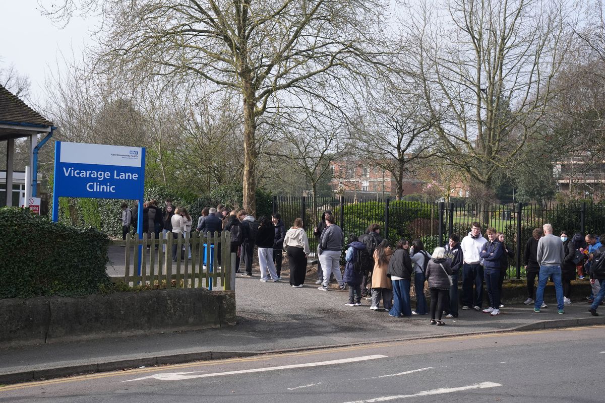 People wait in line outside a meningitis vaccination hub at the Vicarage Lane Clinic in Ashford, Kent