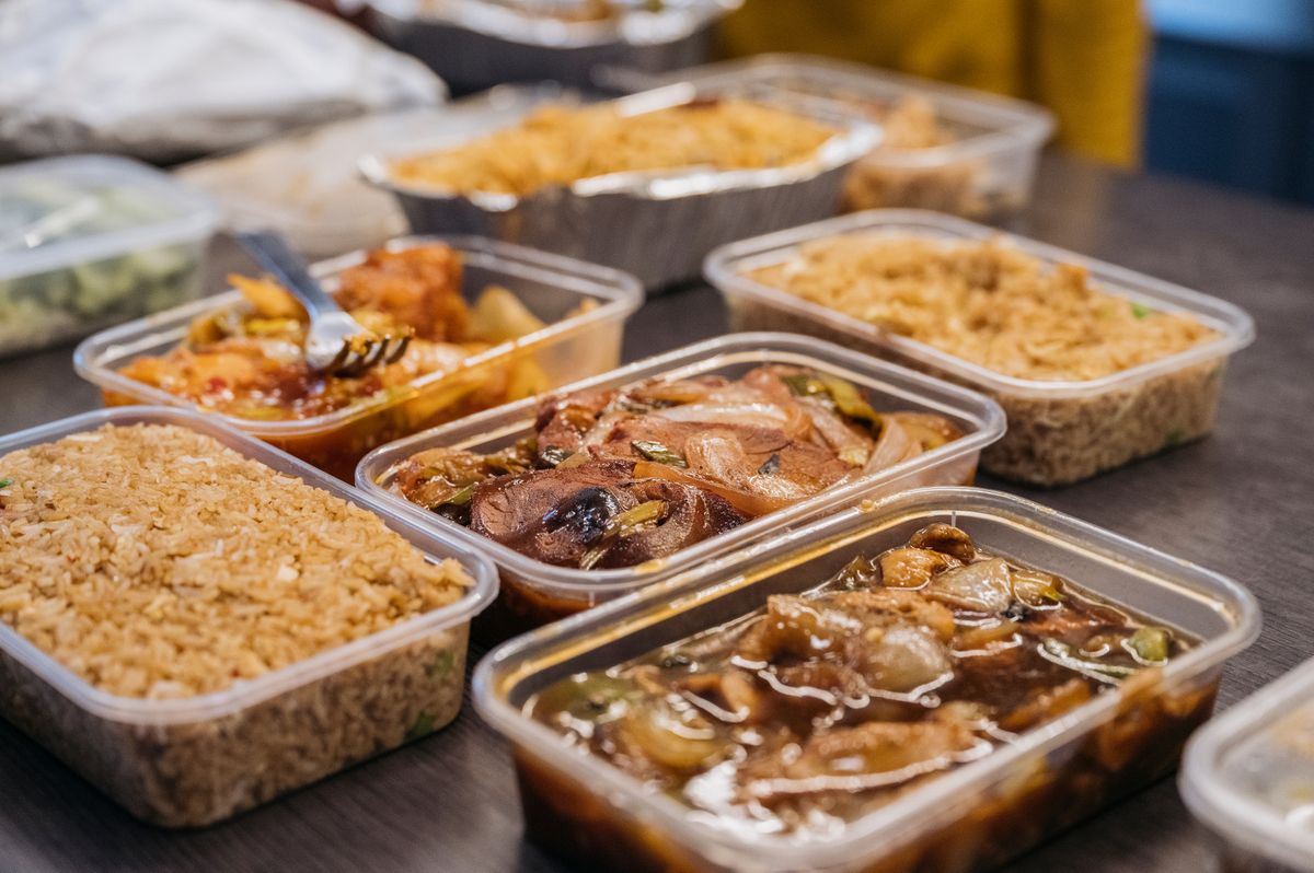 Close-up of fried rice, meat, and vegetables in plastic containers sitting on kitchen island in family home.