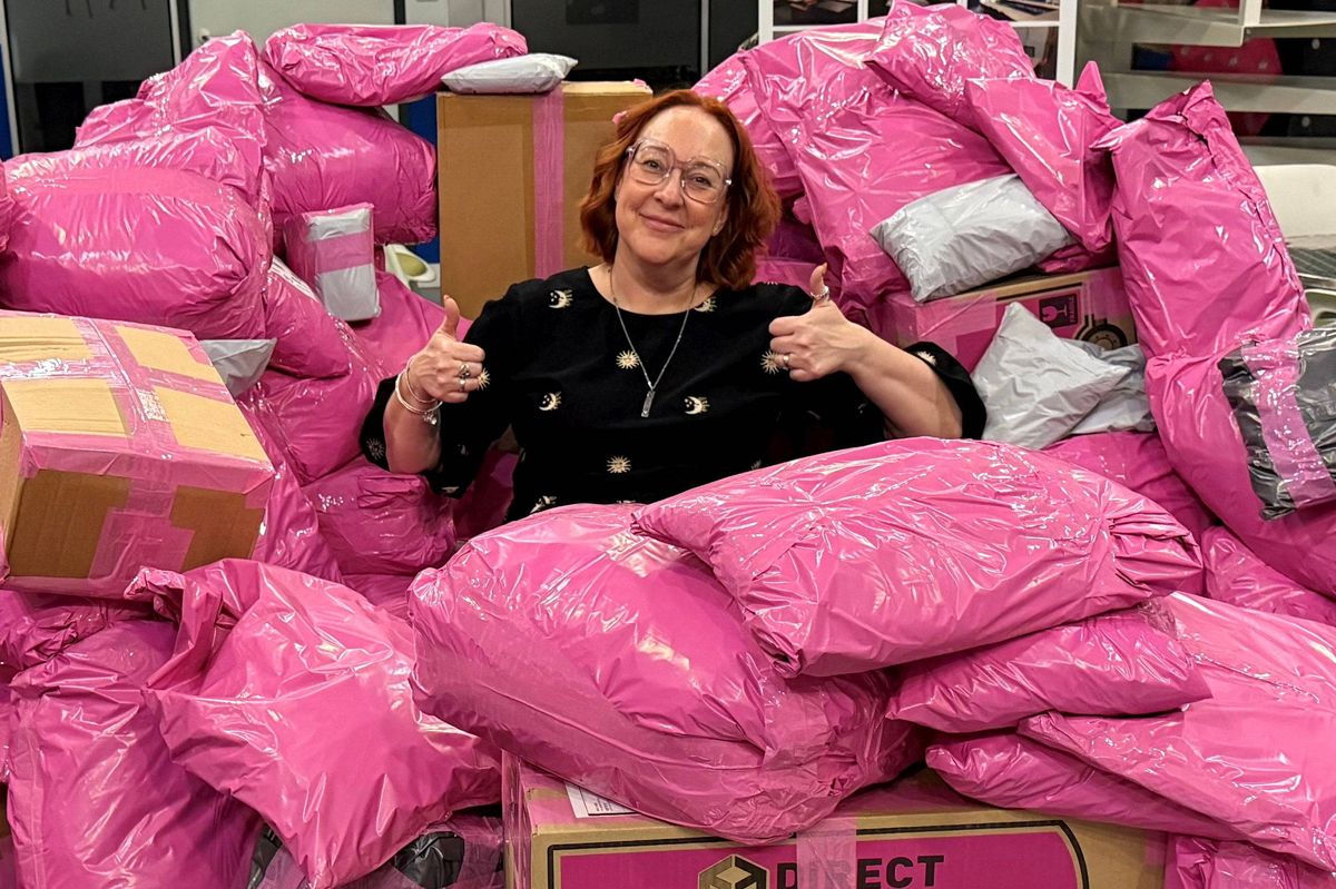 An individual standing amidst a large collection of pink plastic bags, with a thumbs-up gesture, surrounded by multiple storage boxes.