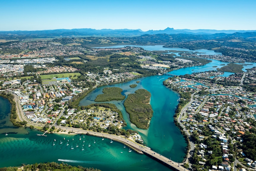 An aerial photo of an urban area with a river through the middle, and a green mountain range in the distance.