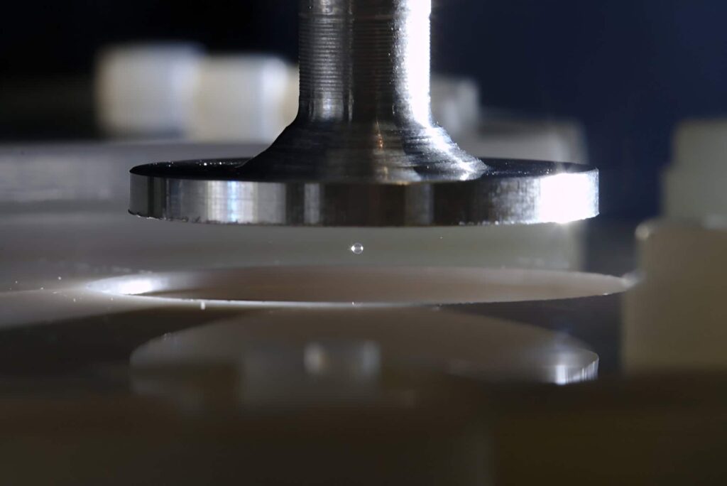 Close-up of a metallic object over a reflective surface with a small clear sphere hovering between them