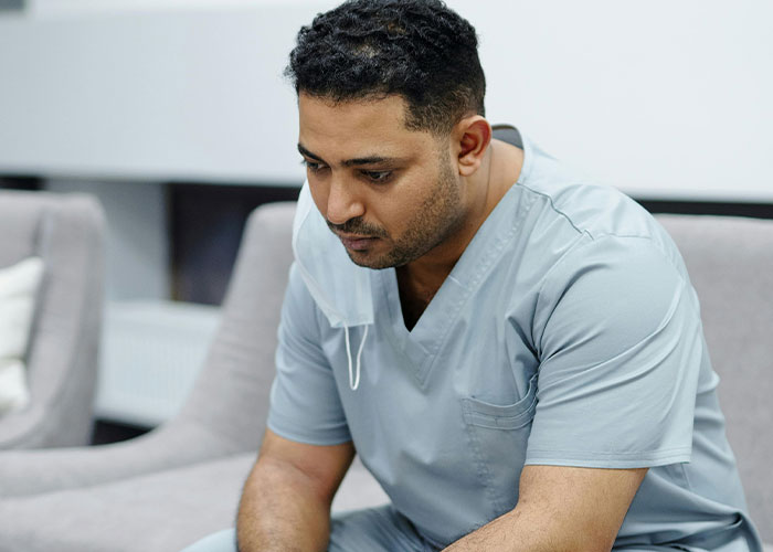 A male medical professional in scrubs sitting thoughtfully on a sofa, revealing medical secrets in a clinical setting.