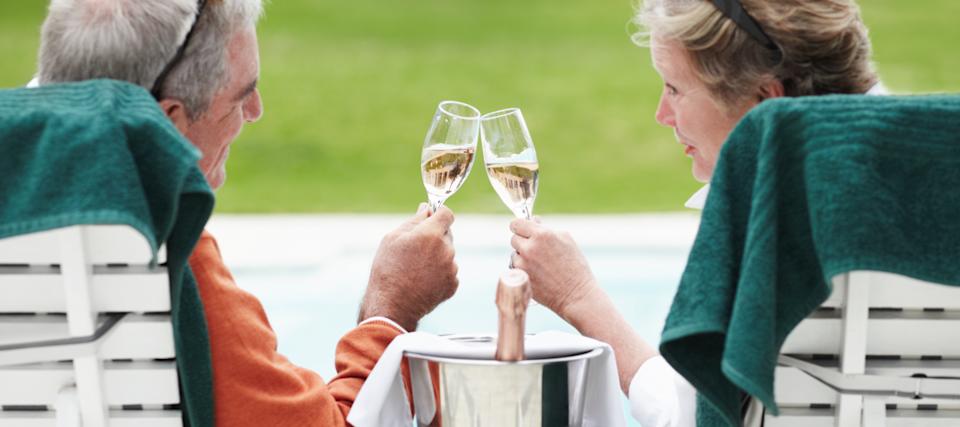 An older couple clink glasses with a champagne bucket between them.
