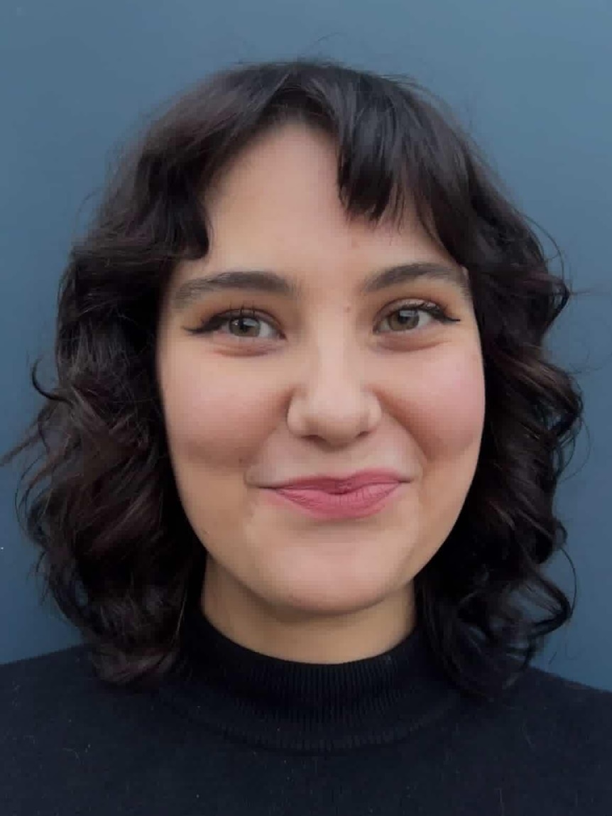 A young woman with wavy dark hair smiles.
