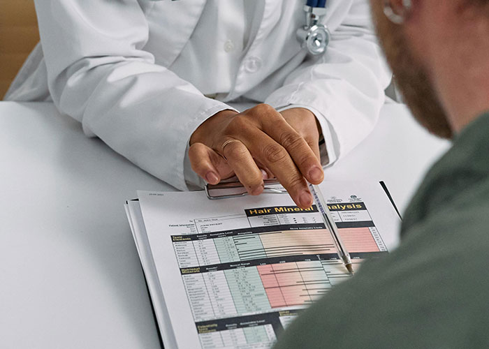 Doctor in white coat pointing at medical report during consultation revealing medical secrets to patient.