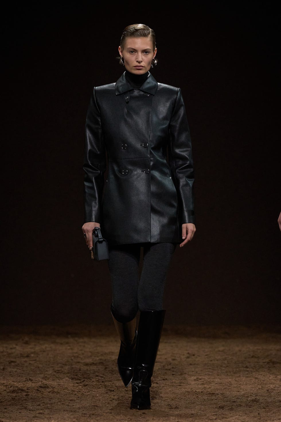 Model showcasing a modern black leather coat during a fashion runway show.
