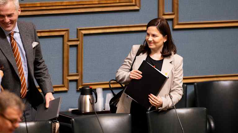 A dark-haired woman smiles while holding a folder.