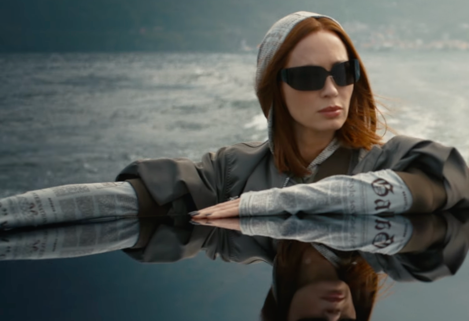 a person with arms extended seated near water with a reflective surface