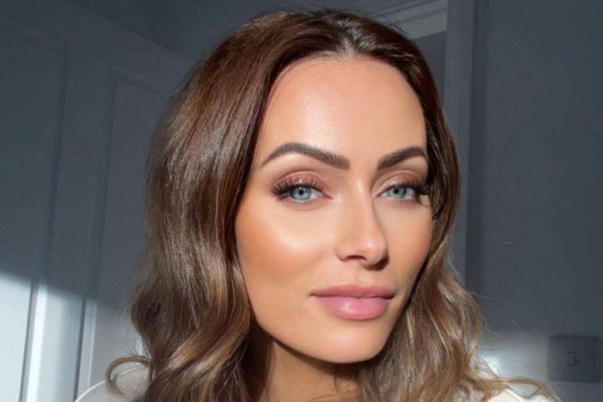 An individual with long, wavy hair and a serious expression is captured in a close-up shot. The subject is illuminated by natural light, with a soft background that enhances facial features.