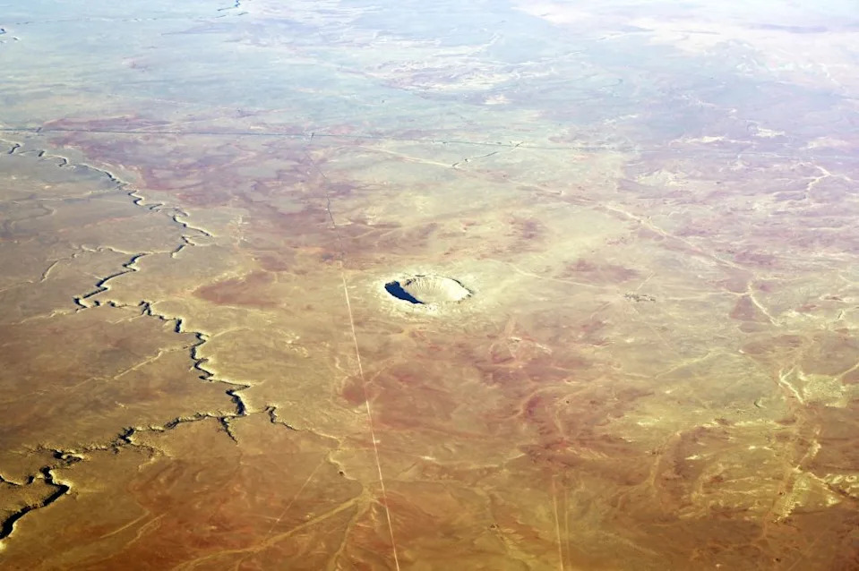 An aerial view of a large crater in the middle of a brown and tan arid landscape