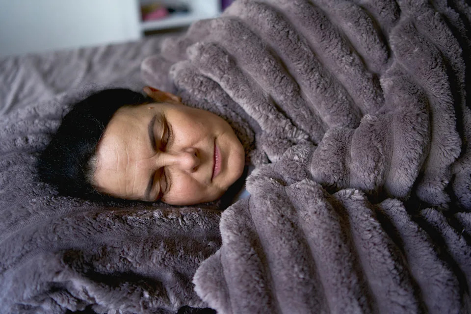 Person sleeping peacefully under a fluffy blanket, head resting on a matching pillow