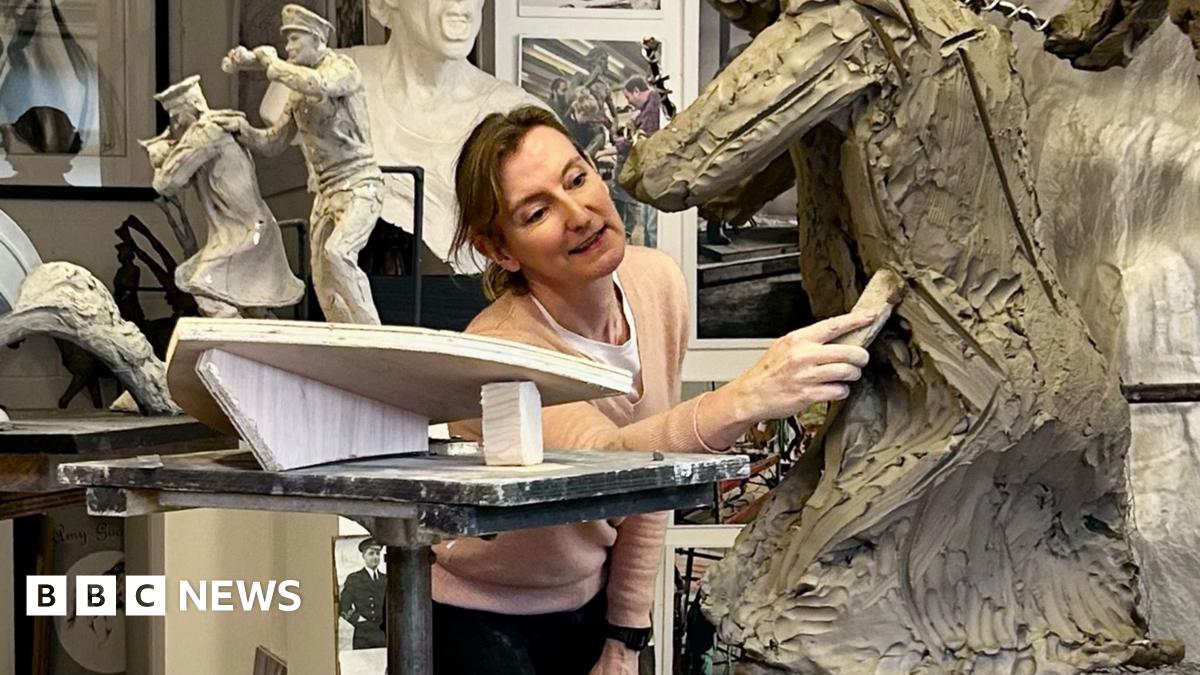 Amy Goodman is pictured in her workshop, using a tool on a statue in progress. Near her are figurines of two men on the prow of a boat, showing how part of the Coastal Forces memorial will look. Photographs of Royal Navy Wrens are positioned in front of her.
