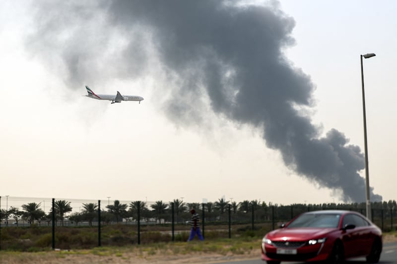 An Emirates Airbus A350 aircraft prepares for landing as a smoke plume rises from an ongoing fire at Dubai International Airport in Dubai on March 16, 2026. Flights were gradually resuming at Dubai airport on March 16, previously the world's busiest for international flights, the airport operator said, after a "drone-related incident" sparked a fuel tank fire nearby, as Iran kept up its Gulf attacks. (Photo by AFP via Getty Images) / 