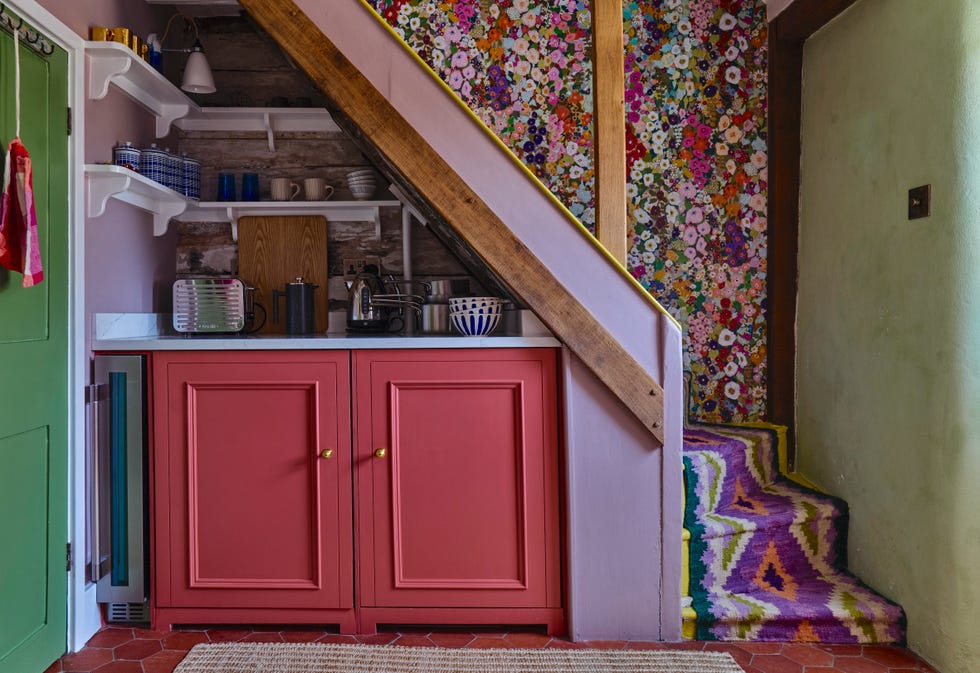 red fitted kitchen units installed under stairs covered in richly patterned carpet