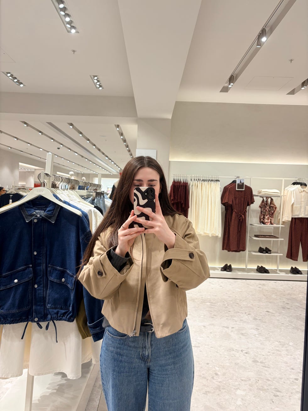 person in a clothing store wearing a beige cropped jacket and blue jeans