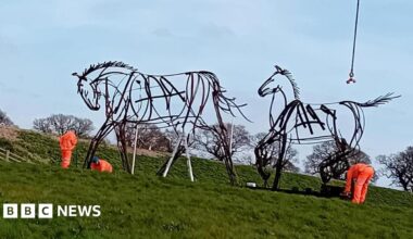 Three workman install two large horst statues. The statues are made of steel and are designed to look as though they have been drawn with pens.