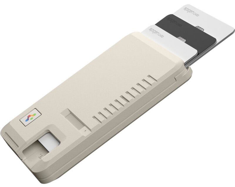 A beige card reader device with three labeled cards partially inserted in separate slots. The cards are white, gray, and black, and the device has a small fingerprint sensor and a colored logo on one end.